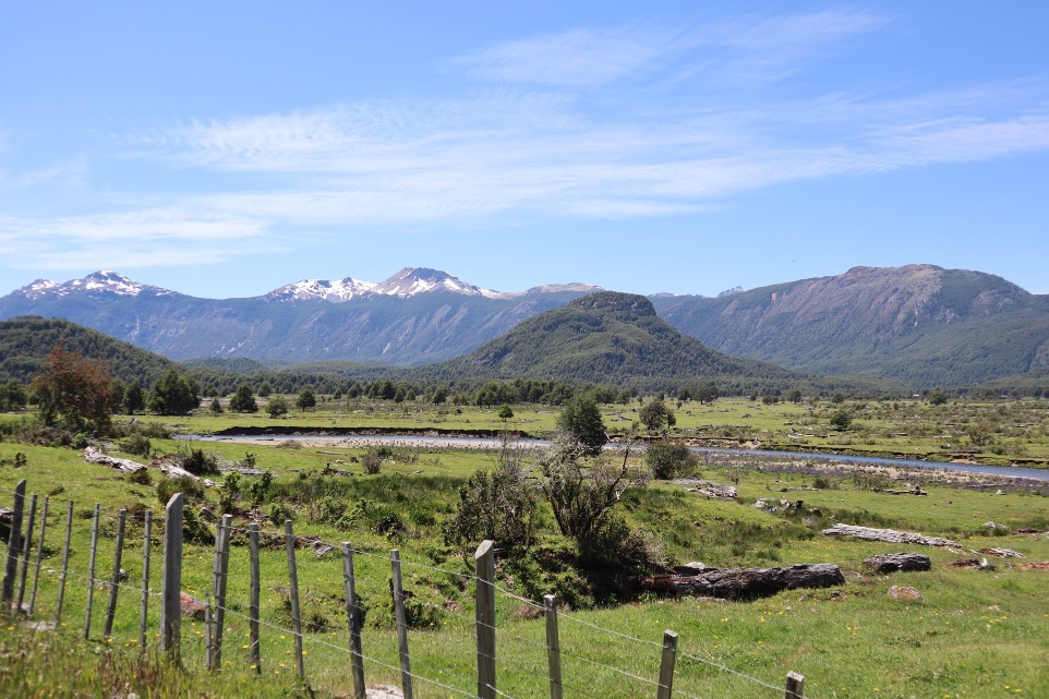 green grass field near mountain under blue sky during daytime