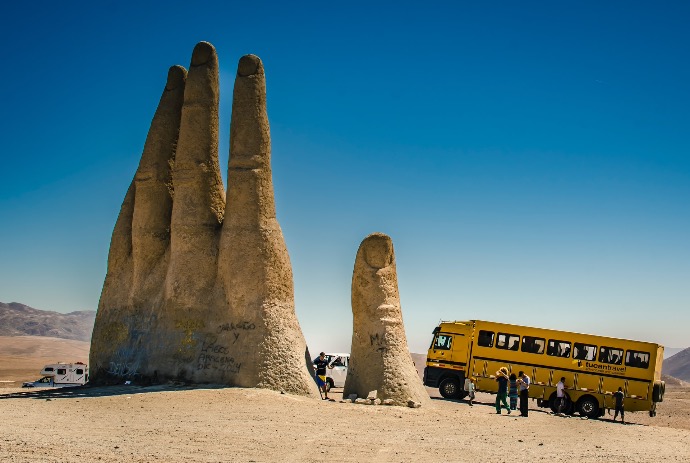 people sitting on brown sand near yellow bus during daytime
